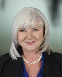 Portrait of Mikki Belliveau, silver-haired and wearing a pearl necklace and black jacket