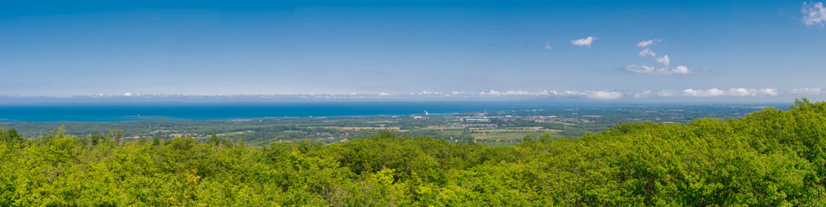 Panorama across forested escarpment slopes to the blue water of Georgian Bay and the Collingwood shoreline